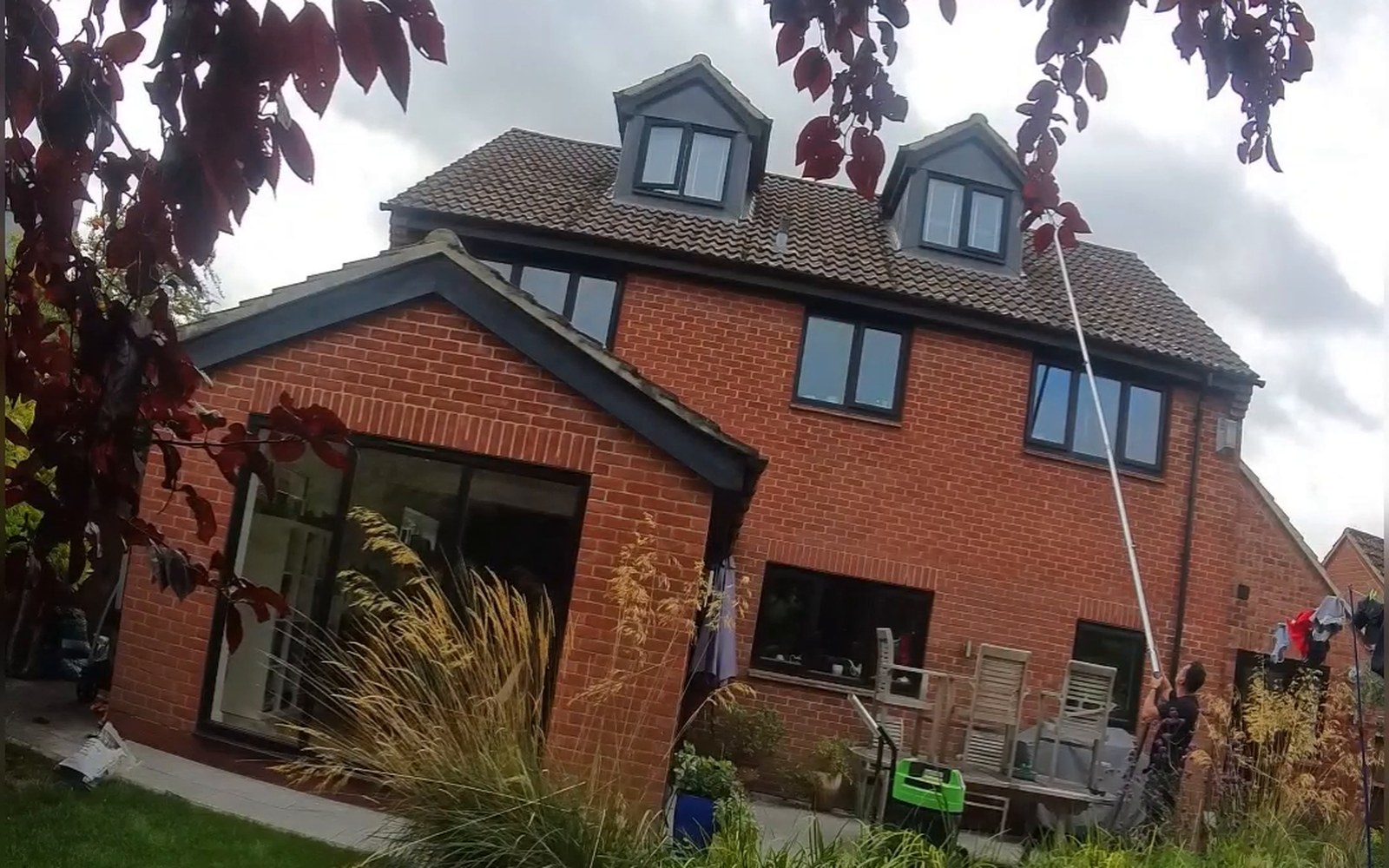 Andrew reaching the high-level gutter beside the dormer windows at the rear of a detached house on Fanshawe Road, Thame, using a gutter vacuum pole from the ground